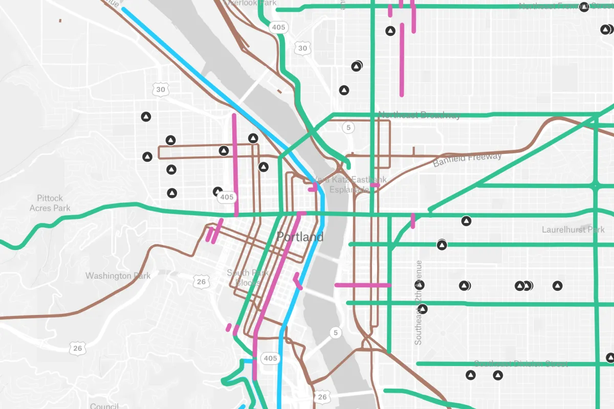 A simplified transit and road network map of Portland, Oregon, showing color-coded routes and infrastructure markers across the city’s grid and Willamette River crossings to assist in urban mobility planning.