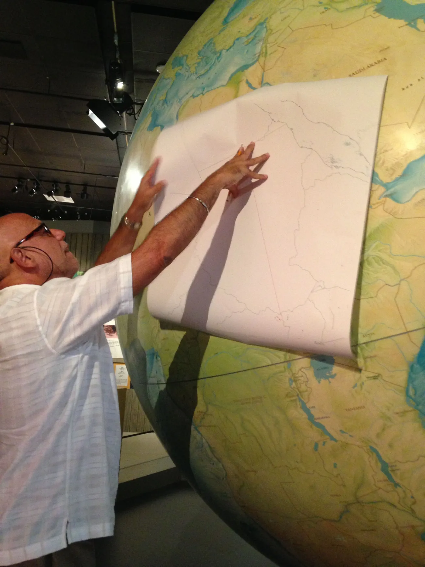 A photo of a man pressing a paper boundary template onto a giant painted globe over East Africa